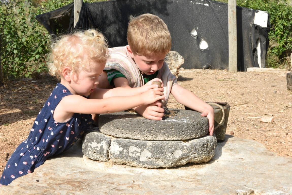 Two children grinding grain with traditional stone mill at Kfar Kedem biblical village